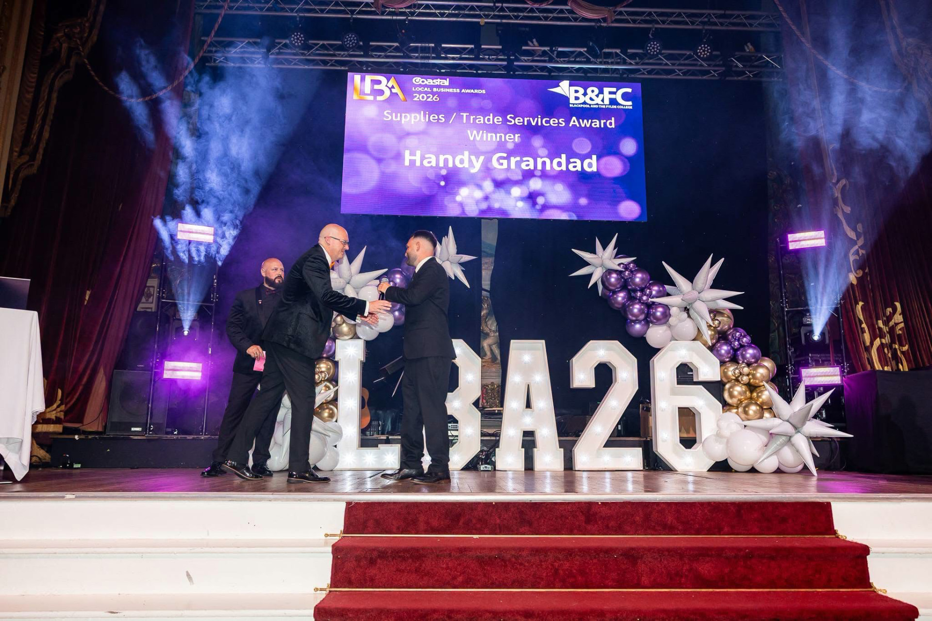 Handshake on stage as Handy Grandad is announced as the Supplies and Trade Services Award winner